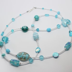 May include: A long, layered necklace with white beads and blue and turquoise glass beads of various shapes and sizes.
