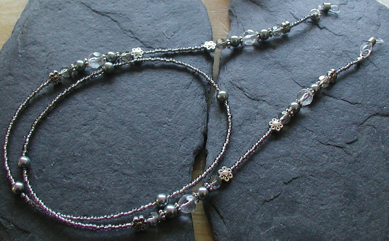 May include: A silver and gray beaded eyeglass chain with clear glass beads and silver flower accents.