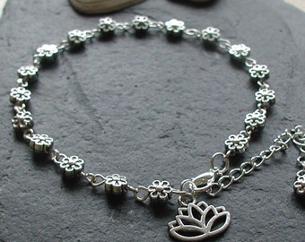 May include: Silver anklet with a delicate chain and small flower charms. The anklet has a lotus flower charm dangling from the clasp.