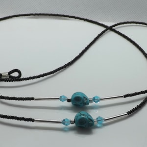 以下が含まれることがあります： 銀色の金属製の留め具とターコイズ色の頭蓋骨のビーズが付いた黒いビーズの眼鏡チェーン