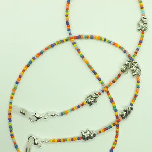 May include: A colorful beaded eyeglass chain with silver elephant charms. The chain is made of small, multi-colored beads and has two silver clasps for attaching to glasses.