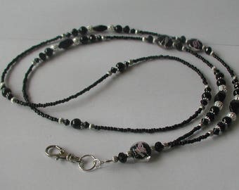 May include: Black and silver beaded lanyard with a pink and black glass bead. The lanyard has a silver lobster clasp.