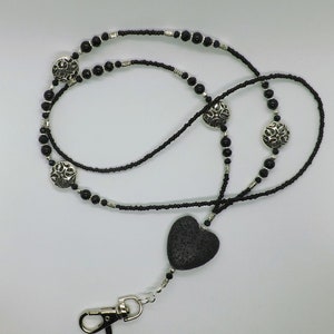 Peut inclure: Lanière noire perlée avec un pendentif en forme de cœur argenté et des perles en filigrane argentées. La lanière est munie d'un clip en métal noir.