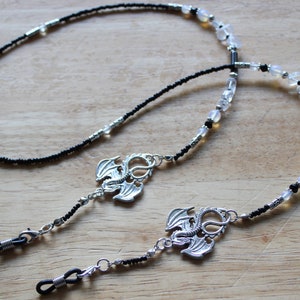 May include: Two black beaded eyeglass chains with silver dragon charms. One chain has clear beads and the other has black beads.