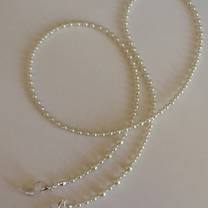 May include: A white pearl beaded eyeglass chain with silver clasps. The chain is approximately 76 cm long and is made of small, round pearls.