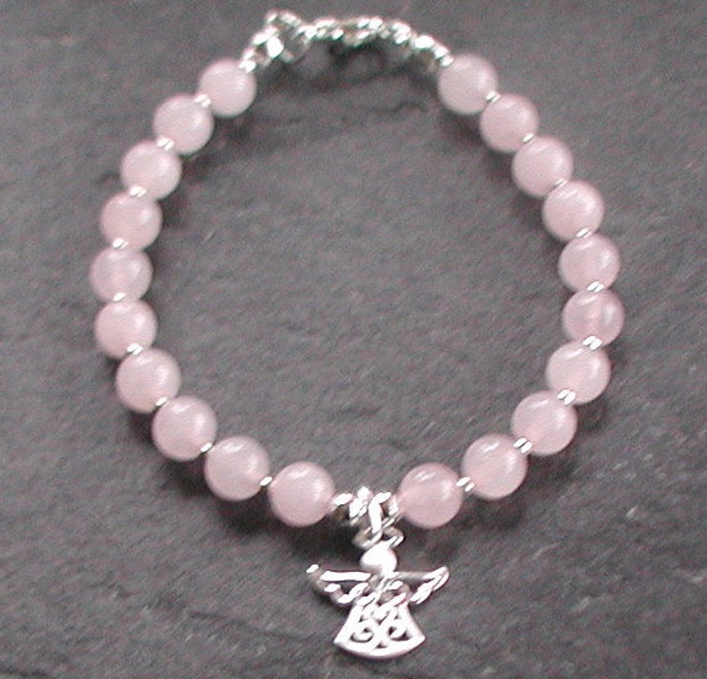 Może przedstawiać: Bransoletka z koralik&oacute;w r&oacute;żowego kwarcu z zawieszką w kształcie anioła ze srebra. Bransoletka wykonana jest z okrągłych koralik&oacute;w i ma srebrną klamrę.