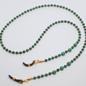 May include: A green malachite and gold beaded eyeglass chain. The chain has two gold clasps with black rubber tips to attach to glasses.