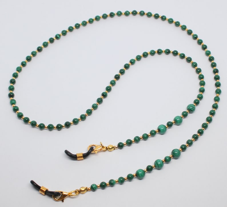 May include: A green malachite and gold beaded eyeglass chain. The chain has two gold clasps with black rubber tips to attach to glasses.