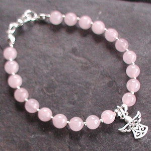 Może przedstawiać: Bransoletka z koralik&oacute;w z r&oacute;żowego kwarcu z zawieszką w kształcie anioła ze srebra. Bransoletka wykonana jest z okrągłych koralik&oacute;w i ma srebrną zapinkę.