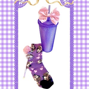 May include: A purple tumbler with a pink bow and a purple sock with cartoon faces and hearts. The sock has a pink pom-pom and a charm. The background is a purple and white gingham pattern.