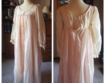 May include: A vintage-style nightgown in soft pink and cream colors. The long-sleeved gown features a gathered bodice, a scoop neckline, and delicate ribbon ties. The sleeves have elastic cuffs with ribbon ties. The gown is displayed on a mannequin.