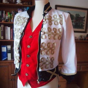 May include: White jacket with gold embroidery and black trim, paired with a red vest. The jacket features decorative gold rope detailing and ornate buttons. The ensemble is displayed on a mannequin.