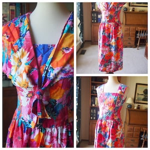 May include: A vibrant floral print dress with a V-neck and bow detail. The dress has a square neckline and a full skirt. The fabric is a mix of pink, orange, blue, and white floral patterns. The dress is a vintage style.