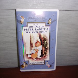 May include: A VHS video cassette featuring the tale of Peter Rabbit and Benjamin Bunny from the Peter Rabbit Collection. The cover features a blue and white illustration of Peter Rabbit holding an umbrella.