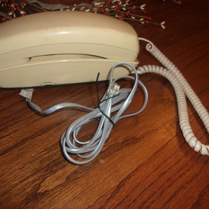 May include: A beige rotary phone with a coiled cord. The phone has a built-in answering machine and a RJ-11 jack.