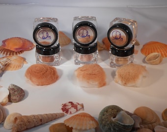 Può includere: Tre barattoli di vetro trasparente con coperchi neri contenenti una polvere marrone chiaro. I barattoli sono impilati uno sopra l'altro. I barattoli sono etichettati con il testo "Siln" e "Cosmetici minerali".