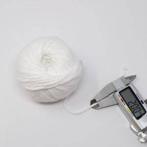 Puede incluir: Una bola de hilo blanco que se mide con un calibre digital. El calibre muestra 2,00 mm.