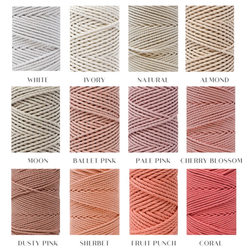 Op de afbeelding: Close-up van 12 spoelen katoenen touw in verschillende tinten wit, beige, roze en koraal. De kleuren zijn gelabeld: Wit, Ivoor, Natuurlijk, Amandel, Maan, Balletroze, Bleekroze, Kersenbloesem, Stofrose, Sorbet, Fruitpunch en Koraal.