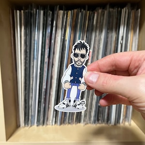 May include: A sticker of a cartoon man wearing a blue and white varsity jacket, blue jeans, and black trainers. He is wearing sunglasses and has a beard. The sticker is on a white background.