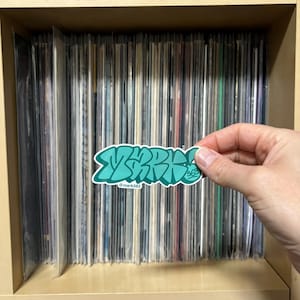 May include: A teal green sticker with the word "ZAP" written in a graffiti style font. The sticker has the text "@mark563" underneath the word "ZAP".