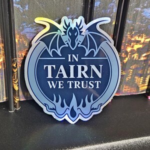 May include: A holographic sticker with a dragon design and the text "In Tairn We Trust".