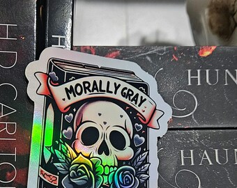 May include: A holographic sticker of a book with a skull and roses. The book has the text "Morally Gray Book Club" on the cover.