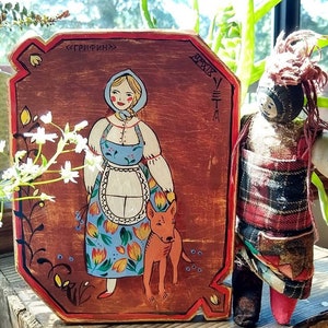 May include: A hand-painted wooden plaque with a folk art style illustration of a woman in a blue dress and a red dog. The plaque has a red border and the text "<ГРИФИН>" and "MMXIX" in black.