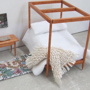 Little Handmade Half Inch to Foot Dollhouse Bed Throw Blanket, 1:24 Scale Miniature Artisan Hand Knit Ivory Cream White Bedspread, Doll House Furniture Bedroom Bedding, Collector Model Home Decor Accent Textile for Traditional Style or Modern Country Farmhouse, Cabin, or Cottage. Styled draped on the corner of a four post bed with white bedspread, with a brocade rug, chair, table with linen mat, and winter landscape painting on the wall.