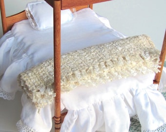 May include: Miniature four-poster bed with white bedding. The bed frame is made of wood and features a white pillow with lace trim. A cream-colored fringed throw blanket rests on the bed. The bed skirt has a ruffled design with lace trim.