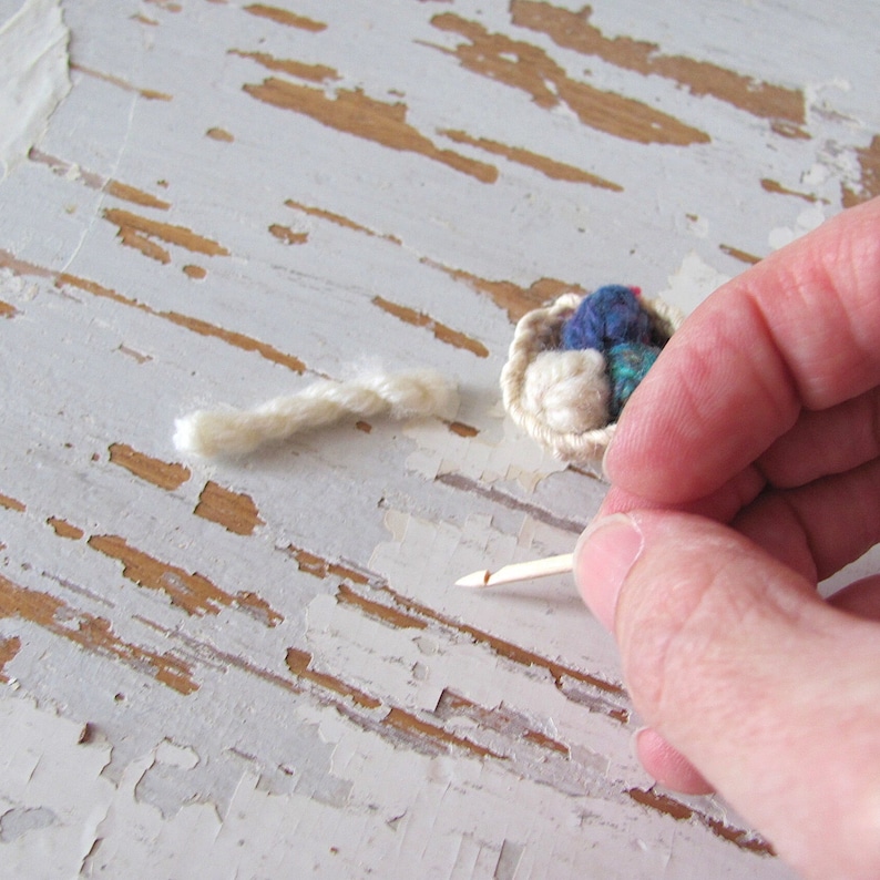 Inch to Foot Scale 1:12 Miniature Dollhouse Wood Crochet Hook Yarn Needle, Roombox Model Collector Textile Fiber Artist Handspinner Gift. Styled with a small white crocheted basket filled with balls of yarn and a skein of yarn. Held by fingers for scale.
