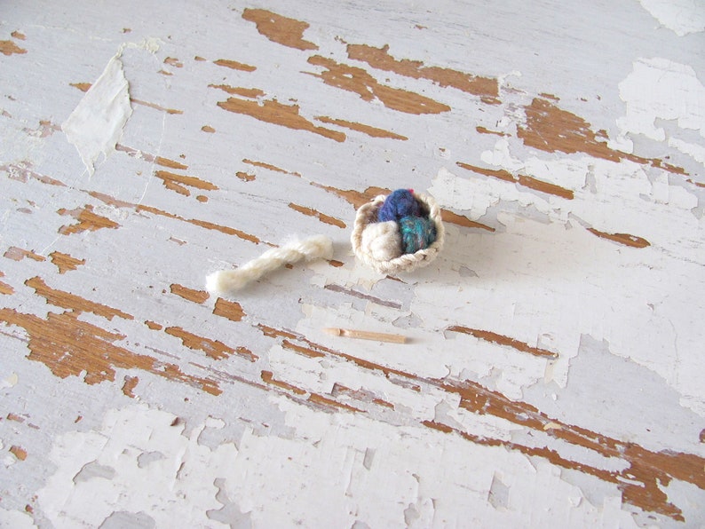 Inch to Foot Scale 1:12 Miniature Dollhouse Wood Crochet Hook Yarn Needle, Roombox Model Collector Textile Fiber Artist Handspinner Gift. Styled with a small white crocheted basket filled with balls of yarn and a skein of yarn.