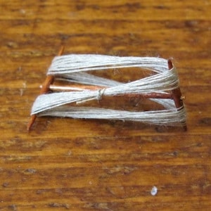 May include: A simple wooden spinning wheel with a spool of white yarn wound around it.