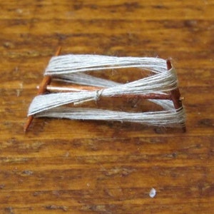 May include: A wooden spinning wheel with white yarn wound around it. The yarn is wrapped around the spokes of the wheel and is ready to be spun into thread.