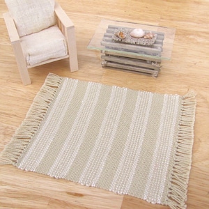 May include: Miniature dollhouse furniture set including a beige and white striped rug with fringe, a small wooden armchair with a beige cushion, and a glass-topped coffee table. The table has a decorative element with shells.