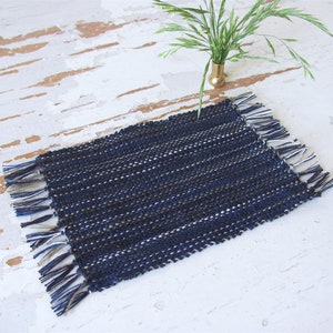 Handcrafted, Inch to Foot Dollhouse Miniature Rug is 1:12 Scale Artisan Hand Loom Woven in Indigo Navy Ocean Blue, Beige, and White Stripe Floor Carpet for Modern Coastal Seaside Nautical Beach House, Cabin Decor Doll House Furniture Accessory. Styled with a green plant in a floor vase.