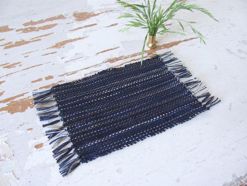 Handcrafted, Inch to Foot Dollhouse Miniature Rug is 1:12 Scale Artisan Hand Loom Woven in Indigo Navy Ocean Blue, Beige, and White Stripe Floor Carpet for Modern Coastal Seaside Nautical Beach House, Cabin Decor Doll House Furniture Accessory. Styled with a green plant in a floor vase.