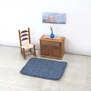 Inch to Foot Dollhouse Miniature Rug, 1:12 Scale Woven Small Indigo Navy Blue and Light Blue Floor Carpet for Modern Coastal Seaside Cottage or Traditional Rustic Nautical Beach Doll House. Styled with a rocking chair, cabinet with a linen runner and blue glass vase with white flowers, a picture of racing sailing ships on the wall.
