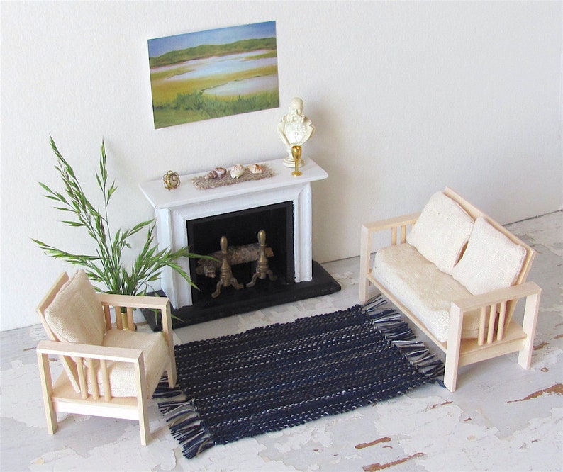 Handcrafted, Inch to Foot Dollhouse Miniature Rug is 1:12 Scale Artisan Hand Loom Woven in Indigo Navy Ocean Blue, Beige, and White Stripe Floor Carpet for Modern Coastal Seaside Nautical Beach House, Cabin Decor Doll House Furniture Accessory. Styled with a chair and couch in front of a fireplace, with a green plant in a floor vase and marsh landscape.
