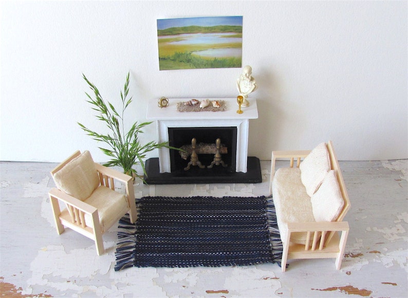 Handcrafted, Inch to Foot Dollhouse Miniature Rug is 1:12 Scale Artisan Hand Loom Woven in Indigo Navy Ocean Blue, Beige, and White Stripe Floor Carpet for Modern Coastal Seaside Nautical Beach House, Cabin Decor Doll House Furniture Accessory. Styled with a chair and couch in front of a fireplace, with a green plant in a floor vase and marsh landscape.