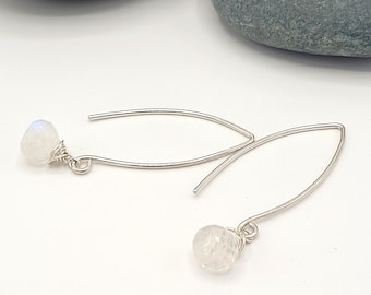 May include: A pair of silver-toned drop earrings. Each earring features a small, faceted, white gemstone at the bottom, connected to a curved wire. The earrings are displayed on a white surface.