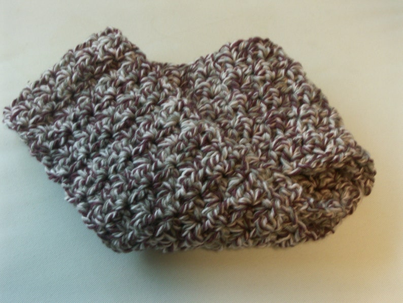 May include: A crocheted hat in a mix of white, grey, and burgundy yarn. The hat features a folded brim and a textured stitch pattern. The hat appears soft and warm, suitable for cooler weather.