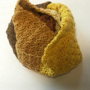 May include: A crocheted scarf in shades of brown, yellow, and gold. The scarf is made of a soft, textured yarn and is folded into a decorative shape.