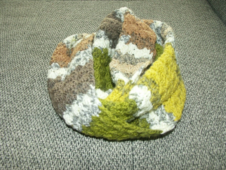May include: A knitted infinity scarf in shades of green, brown, and white. The scarf is made of a soft, textured yarn and has a simple, elegant design.