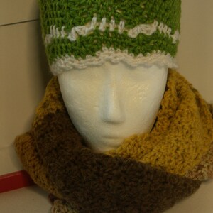 May include: A green crocheted hat with a white crocheted bow and a brown and yellow crocheted scarf.