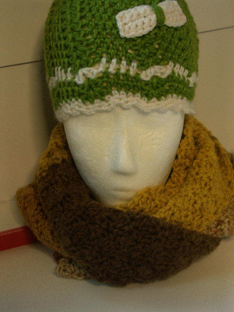 May include: A green crocheted hat with a white crocheted bow and a brown and yellow crocheted scarf.