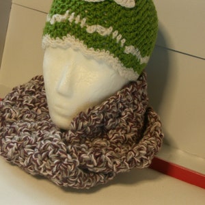 May include: A green and white crocheted beanie hat and a matching infinity scarf. The scarf is a mix of brown, white, and burgundy yarn. The hat is on a mannequin head.