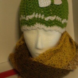 May include: A green crocheted hat with a white crocheted bow and a brown and yellow crocheted scarf.