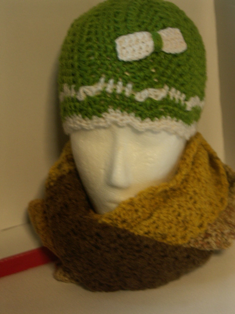 May include: A green crocheted hat with a white crocheted bow and a brown and yellow crocheted scarf.