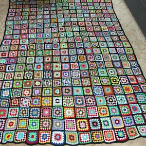 Puede incluir: Una manta de ganchillo colorida con fondo negro y cuadrados de varios colores, incluyendo verde, rojo, azul y amarillo.
