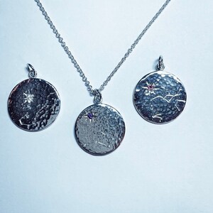 May include: Three silver necklaces with round pendants featuring a star and constellation design. The pendants have a hammered texture and are adorned with small gemstones.